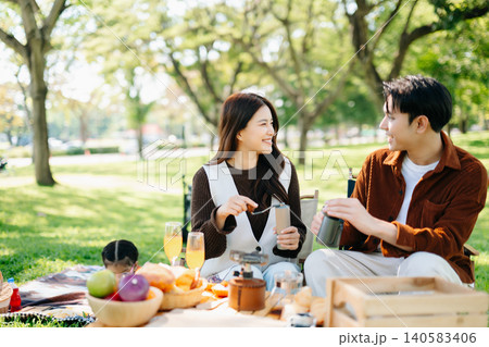 Loving couple preparing coffee together during a picnic in a sunny green park. A warm and candid outdoor lifestyle moment filled Loving couple preparing coffee together during a picnic in a sunny green park. A warm and candid outdoor lifestyle moment filled 140583406