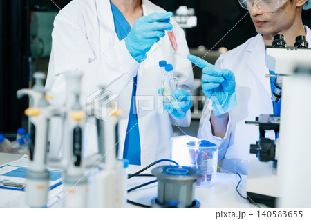 Team of scientists analyzing blue liquid samples in a modern lab, showcasing biotechnology, chemistry, and medical research Team of scientists analyzing blue liquid samples in a modern lab, showcasing biotechnology, chemistry, and medical research 140583655