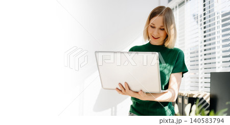 Business woman standing and working on a laptop in a bright modern office with greenery. Business woman standing and working on a laptop in a bright modern office with greenery. 140583794