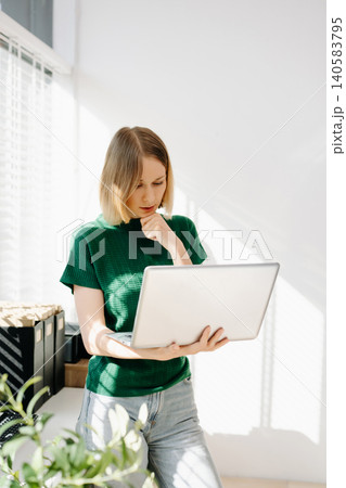 Business woman standing and working on a laptop in a bright modern office with greenery. 140583795
