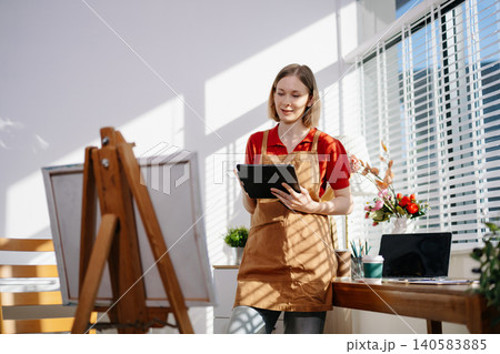 A focused female artist holding her coffee while sketching ideas in her sunlit studio, capturing creativity, peaceful workflow, and an inspiring artistic routine. 140583885