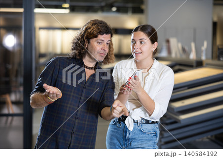 Married couple is actively discussing and comparing prices in a smartphone with prices on price tags in hardware and plumbing store Married couple is actively discussing and comparing prices in a smartphone with prices on price tags in hardware and plumbing store 140584192