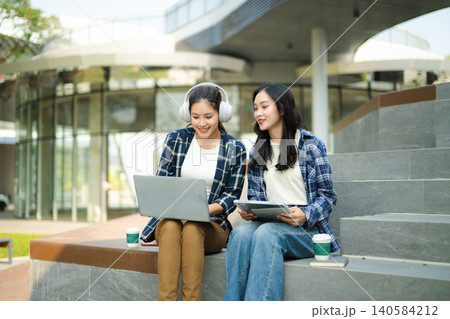 Attractive and beautiful young Asian female college students look at and study insights and biology on a laptop and record in a notebook at the outside Attractive and beautiful young Asian female college students look at and study insights and biology on a laptop and record in a notebook at the outside 140584212