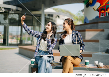 Young Asian women using laptop online meeting outdoors. Remote teamwork, digital communication, education and modern lifestyle with technology concept. Young Asian women using laptop online meeting outdoors. Remote teamwork, digital communication, education and modern lifestyle with technology concept. 140584266