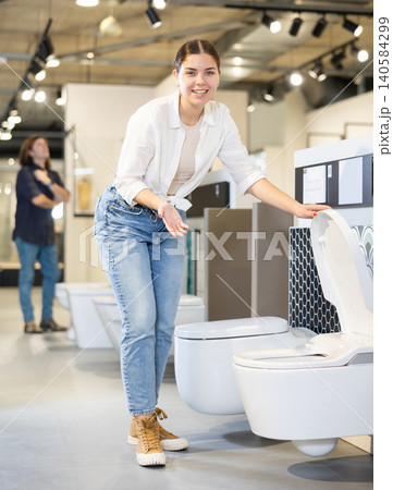 in plumbing department, female buyer checks for defects of toilet before purchasing toilet pan 140584299