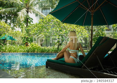 Woman enjoys tranquility by the poolside in a lush garden Woman enjoys tranquility by the poolside in a lush garden 140584317