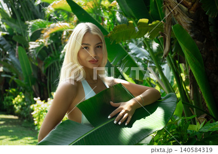 Woman confidently holds a large leaf in a garden Woman confidently holds a large leaf in a garden 140584319