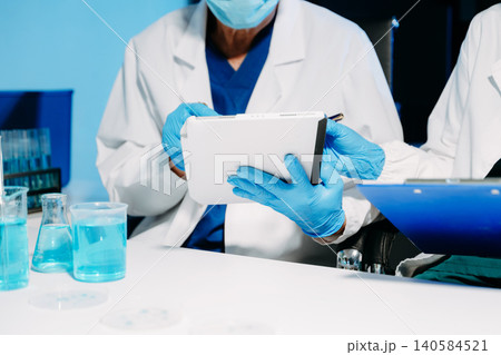 scientists in lab coats conducting research, handling glassware, and working with chemicals in a modern, high tech laboratory. 140584521
