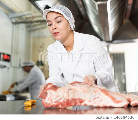 Female butcher preparing raw pork ribs for sale in butchery Female butcher preparing raw pork ribs for sale in butchery 140584530