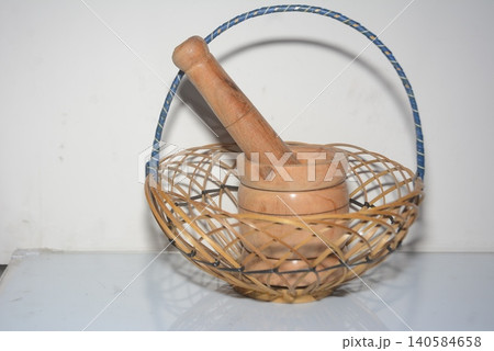 Small wooden mortar and pestle inside an empty woven wicker basket with handmade Small wooden mortar and pestle inside an empty woven wicker basket with handmade 140584658