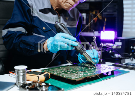 Senior technician performing PCB soldering and diagnostics with multimeter in electronics lab, showcasing hardware engineering 140584781