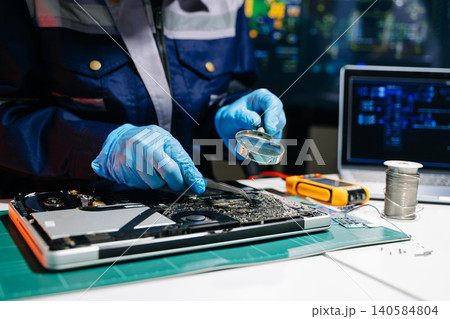 Technician inspecting laptop motherboard using magnifying glass in electronics repair lab, highlighting computer diagnostics, hardware maintenance, engineering Technician inspecting laptop motherboard using magnifying glass in electronics repair lab, highlighting computer diagnostics, hardware maintenance, engineering 140584804
