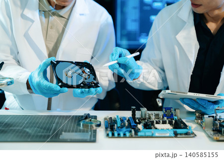 Engineers examining hard drive and motherboard in a technology lab, focusing on data storage, cybersecurity, diagnostics, and computer hardware repair 140585155