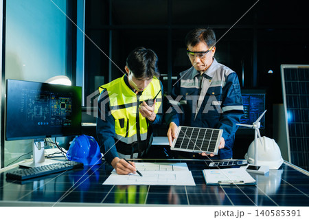 Engineers designing renewable energy project using wind turbine model and solar panels while reviewing digital blueprint. Concept of clean power, sustainability Engineers designing renewable energy project using wind turbine model and solar panels while reviewing digital blueprint. Concept of clean power, sustainability 140585391