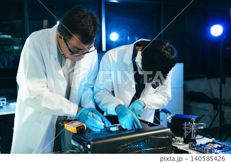 Engineers testing computer hardware with multimeter inside technology laboratory. Electronics repair, motherboard diagnostics 140585426