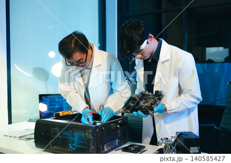 Engineers testing computer hardware with multimeter inside technology laboratory. Electronics repair, motherboard diagnostics Engineers testing computer hardware with multimeter inside technology laboratory. Electronics repair, motherboard diagnostics 140585427