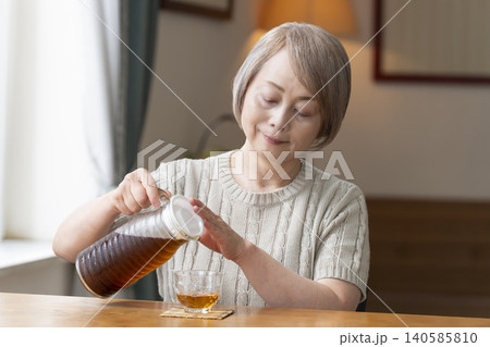 リビングで麦茶を注いで飲むシニア女性 リビングで麦茶を注いで飲むシニア女性 140585810