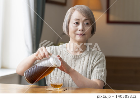 リビングで麦茶を注いで飲むシニア女性 リビングで麦茶を注いで飲むシニア女性 140585812