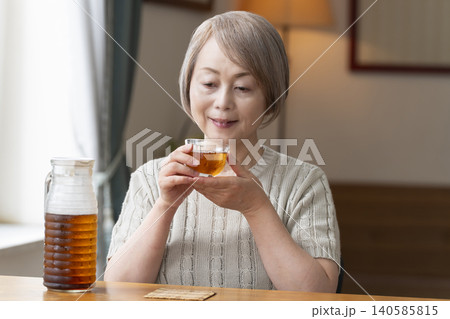 リビングで麦茶を注いで飲むシニア女性 リビングで麦茶を注いで飲むシニア女性 140585815