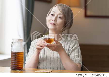 リビングで麦茶を注いで飲むシニア女性 リビングで麦茶を注いで飲むシニア女性 140585816