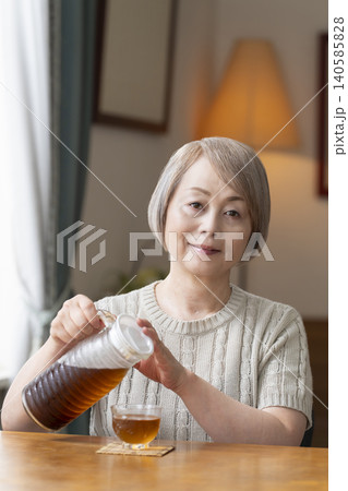 リビングで麦茶を注いで飲むシニア女性 リビングで麦茶を注いで飲むシニア女性 140585828
