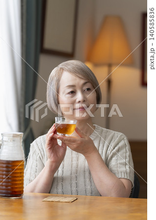 リビングで麦茶を注いで飲むシニア女性 140585836