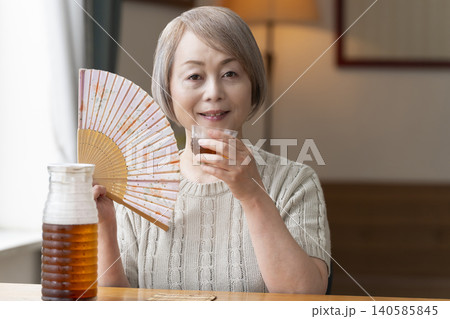 リビングで麦茶を注いで飲むシニア女性 リビングで麦茶を注いで飲むシニア女性 140585845
