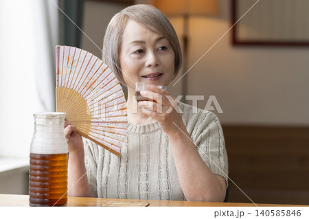 リビングで麦茶を注いで飲むシニア女性 リビングで麦茶を注いで飲むシニア女性 140585846