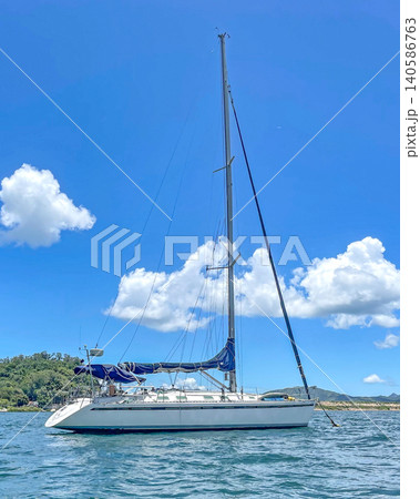 White sailboat with blue sails glides across the sparkling blue ocean under a cloudy sky 140586763