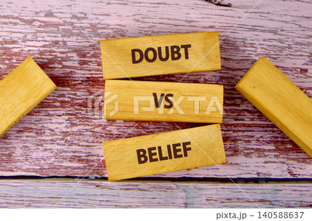 Two wooden blocks with the words doubt and belief sit on a pink wooden surface, illustrating a comparison between two contrasting ideas at a specific time Two wooden blocks with the words doubt and belief sit on a pink wooden surface, illustrating a comparison between two contrasting ideas at a specific time 140588637