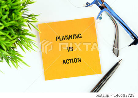 A bright yellow sticky note sits on a clean surface, boldly stating planning vs action, accompanied by glasses and a pen, promoting productivity and focus 140588729