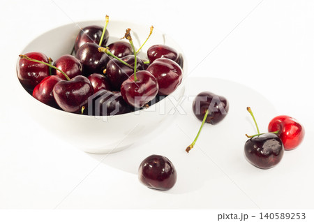 Ripe black sweet cherries on a plate and against a white background. 140589253