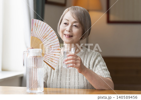 熱中症対策にリビングで水を飲むシニア女性 熱中症対策にリビングで水を飲むシニア女性 140589456