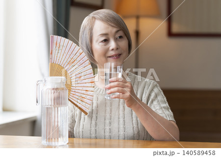 熱中症対策にリビングで水を飲むシニア女性 熱中症対策にリビングで水を飲むシニア女性 140589458