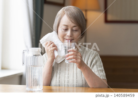 熱中症対策にリビングで水を飲むシニア女性 熱中症対策にリビングで水を飲むシニア女性 140589459