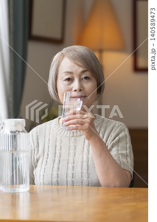 熱中症対策にリビングで水を飲むシニア女性 熱中症対策にリビングで水を飲むシニア女性 140589473