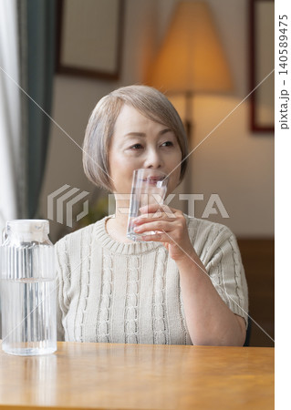 熱中症対策にリビングで水を飲むシニア女性 140589475