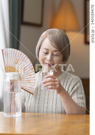 熱中症対策にリビングで水を飲むシニア女性 熱中症対策にリビングで水を飲むシニア女性 140589476