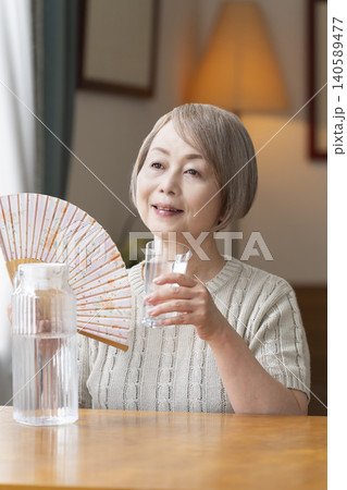 熱中症対策にリビングで水を飲むシニア女性 熱中症対策にリビングで水を飲むシニア女性 140589477