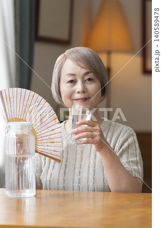 熱中症対策にリビングで水を飲むシニア女性 熱中症対策にリビングで水を飲むシニア女性 140589478