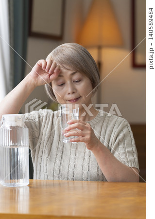 熱中症対策にリビングで水を飲むシニア女性 140589484