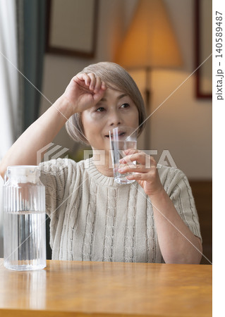 熱中症対策にリビングで水を飲むシニア女性 140589487