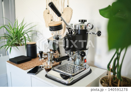 Home barista station with manual lever espresso machine, single dose grinder, and a smartphone on the counter. 140591278