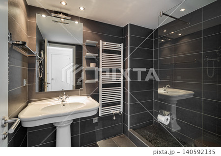 Modern bathroom with sleek black tiles, a white sink, and a glass shower. Bright lighting enhances the contemporary design. Modern bathroom with sleek black tiles, a white sink, and a glass shower. Bright lighting enhances the contemporary design. 140592135