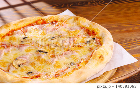 Delicious pizza with cheese, ham, and mushrooms served on a wooden table Delicious pizza with cheese, ham, and mushrooms served on a wooden table 140593065