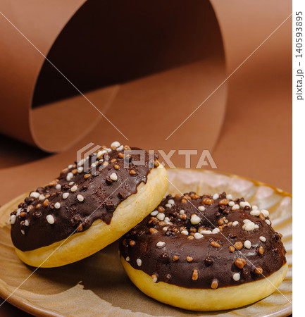 Donuts with chocolate frosting and sprinkles on a plate in a warm setting Donuts with chocolate frosting and sprinkles on a plate in a warm setting 140593895