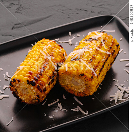 Grilled corn served on a black plate with cheese on top 140593917