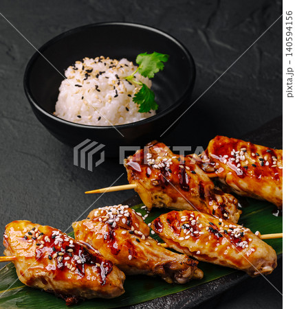 Grilled chicken skewers served with rice and sesame seeds on a dark surface Grilled chicken skewers served with rice and sesame seeds on a dark surface 140594156