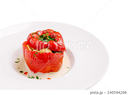 Stuffed red pepper with herbs served on a white plate in a kitchen setting 140594206