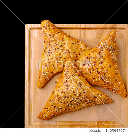 Freshly baked triangle pastries on a wooden tray with sesame seeds on top Freshly baked triangle pastries on a wooden tray with sesame seeds on top 140594227
